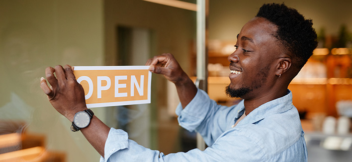 Man holding open sign in front of business
