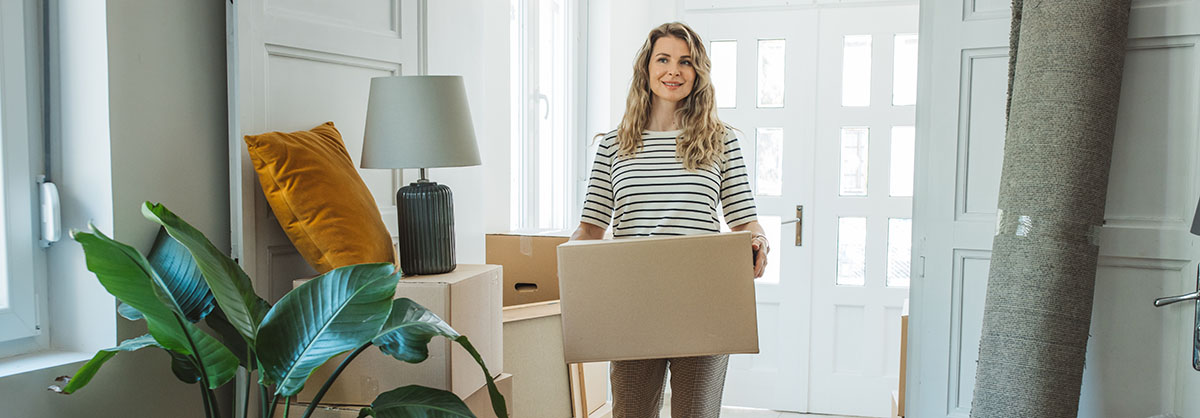 Woman carrying a moving box entering her home.