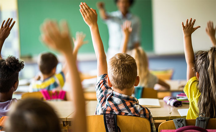 children raising their hands in a classroom