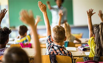 children raising their hands in a classroom