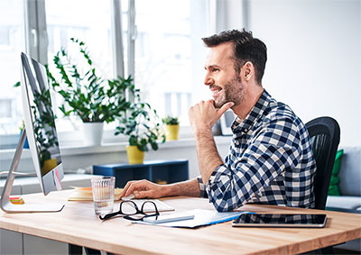 Man seated at his desk looking at computer monitor.