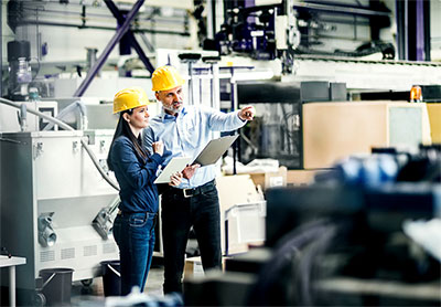 Man and woman wearing hardhats look at machinery.