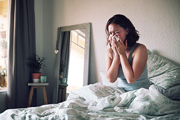 Sick woman in bed blowing nose into tissue.