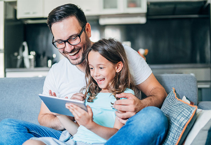 Little girl sitting in her father's lap on a tablet.