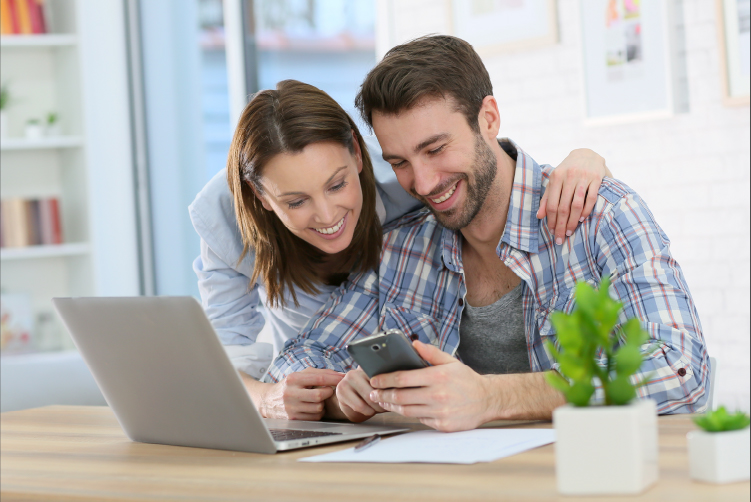 Young couple looking at a cell phone and laptop together.