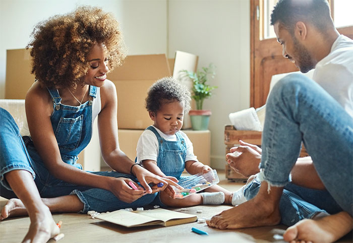 Parents playing with young child on living room floor.