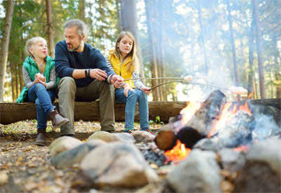 Father and daughters roasting marshmallows over campfire.