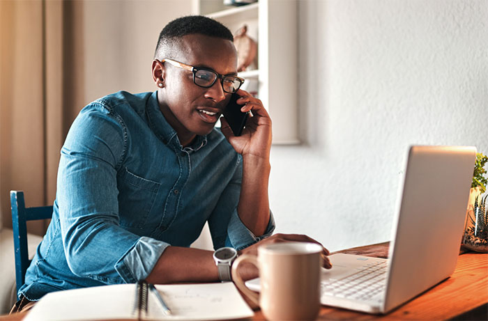 Man talking on phone and using laptop at the same time.