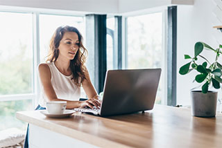 Woman sitting at table with laptop and coffee.