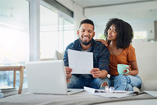 Happy couple on couch looking at bank statement.