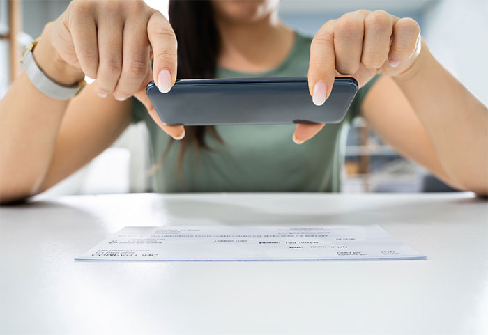 Woman using smartphone camera to take picture of check and use mobile deposit.