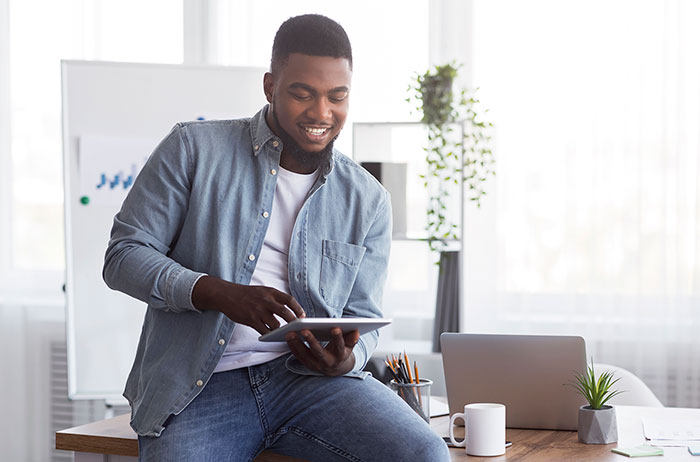 Young man sitting on desk using tablet computer.