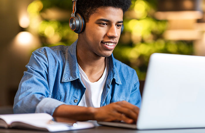 Teenage boy listening to music and working on laptop.