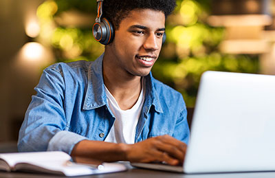 Teenage boy listening to music and working on laptop.